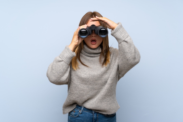 Teenager girl with sweater over isolated blue background with black binoculars, Photo from Adobe Stock by luismolinero